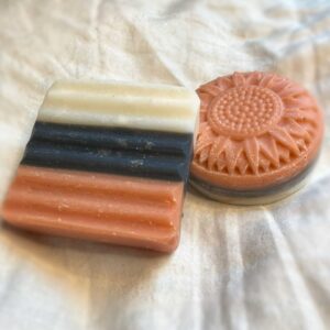 a three color layered bar of soap, one square the other a daisy, in pink, black, and white stripes. It smells like Licorice and looks like All Sorts candies